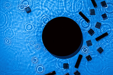 Abstract black geometric figures composition on transparent blue clear calm water texture with splashes. Flat lay cosmetic mockup podium for product presentation. Water waves in sunlight, copy space.