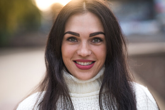 Portrait of a young, happy and attractive Caucasian brunette girl wearing a white sweater.