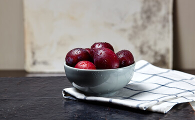 Ripe red plums in bowl with water drops. Juicy fruit on wooden background, closeup. Healthy food on dark kitchen table