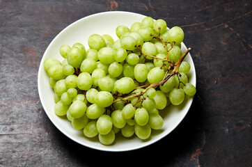 Branch of ripe green grape on plate. Juicy grapes on wooden background, closeup. Grapes on dark kitchen table with copy space