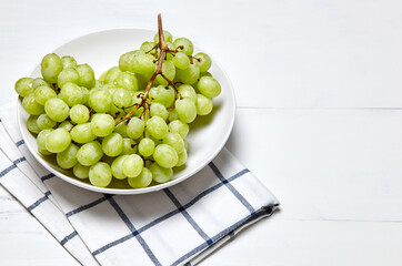 Branch of ripe green grape on plate with water drops. Juicy grapes on wooden background, closeup. Grapes on white kitchen table with copy space