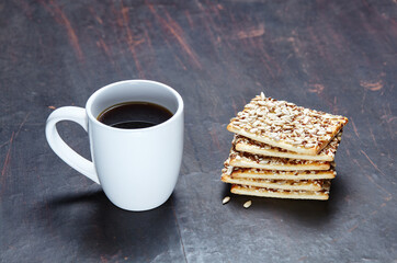 White cup with coffee and crunchy crispbread on a wooden background, closeup. Tasty breakfast, morning routine concept