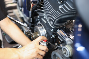 Master locksmith puffs liquid on motorcycle engine in garage closeup