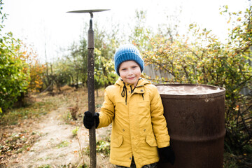 Fototapeta na wymiar Little boy in autumn with garden hoe, planting and gardening, outdoors. Cottagecore concept. Idea of living on farm
