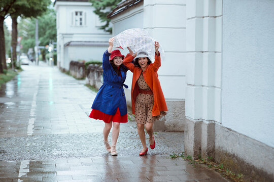 Surprised female tourists holding city map over head while running during rain