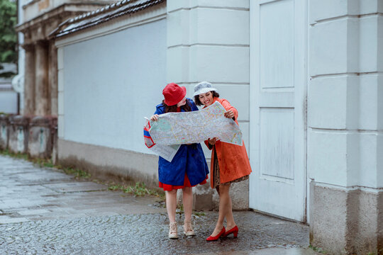 Smiling female tourists sharing map by building on footpath