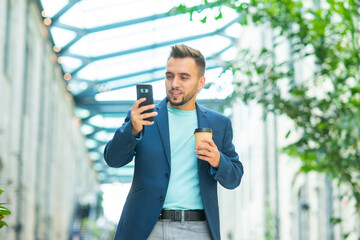 A young successful businessman is working outdoor using smartphone. Man in a casual wear. Business, freelance and remote work.