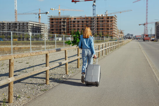 Woman with plant and wheeled luggage walking on road