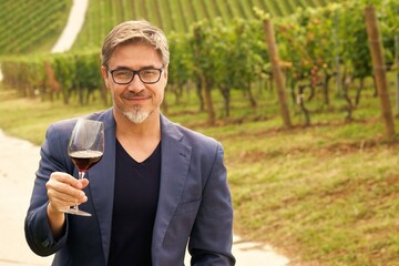 Portrait of happy man in vineyard with glass of red wine. Vintner, agricultural entrepreneur, owner.