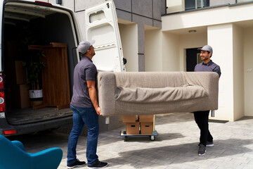 Male delivery coworkers unloading sofa from moving van near house