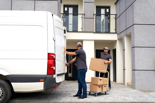 Man looking at colleague holding cardboard box in front of house