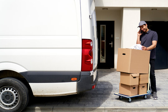 Delivery man talking on smart phone while checking documents near moving van