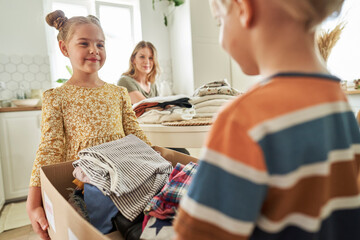 Children carrying donation box with mother in background at home