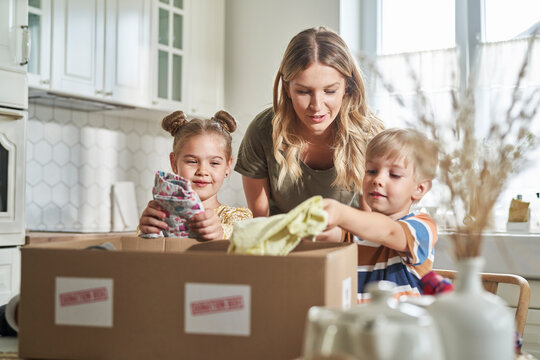 Woman talking with children packing clothes in donation box at home