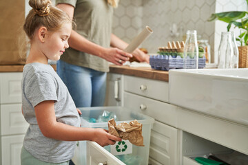 Girl collecting garbage in recycling bin at home