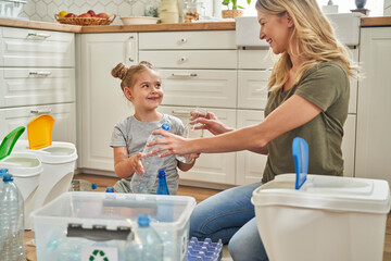 Smiling mother and daughter separating garbage together at home