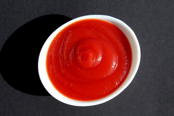 Tomato sauce lies in a white plate on a black background.