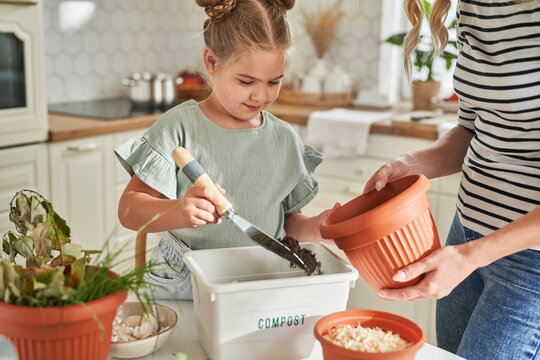 Girl filling compost in flower pot with mother at home