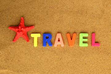 On the beach sand is written a word of bright letters the word travel.