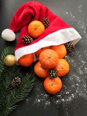 Fototapeta na wymiar Christmas tangerines in a Santa hat on an black background, Christmas fruits, festive symbol, Merry Christmas, New Year and tangerines