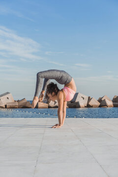 Woman practicing Vrischikasana on boardwalk