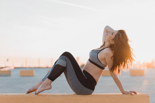 Woman in sports clothing sitting on retaining wall during sunset