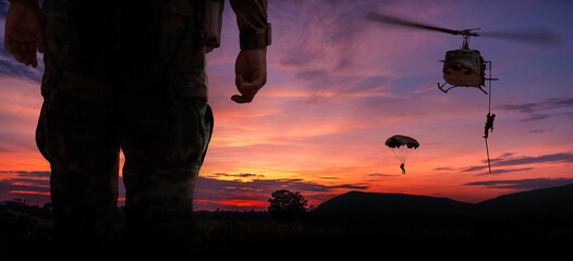 Silhouette back side view soldier paarachute and helicopter soldier under army training and big tree at sunset mountain twilight sky background. © APchanel