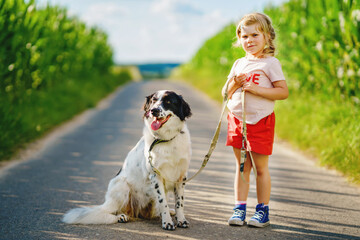 Cute little preschool girl going for a walk with family dog in nature. Happy smiling child having fun with dog, run and hugging. Happy family outdoors. Friendship and love between animal and kids