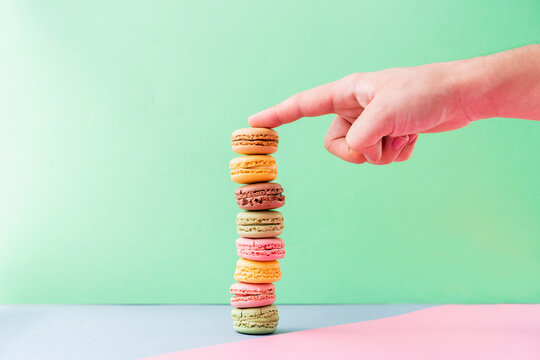 Hand of young man touching stack of pastel colored macaroon cookies