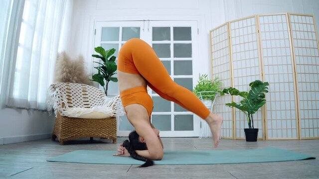 Asian women practicing headstand and yoga at home, with sunshine streaming in through the window.