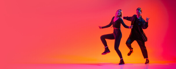 Attractive young man and woman dancing hip-hop isolated on gradient pink studio background in neon...