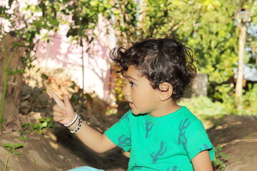 An Indian resident small child looking at a distant object with the gesture of his hand and finger. little indian hindu boy wearing green t-shirt and playing in the garden outside