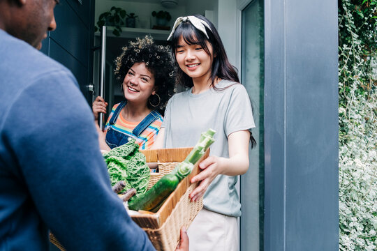 Male delivery person delivering fresh vegetable to women at doorway