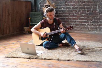 Man acoustic guitar sitting floor with laptop and headphones playing singing song online music...