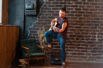 Fototapeta premium Man with acoustic guitar against brick wall playing music singing songs enjoy life Medium shoot