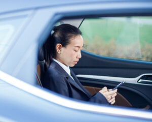 Close up portrait of a young business woman using mobile phone in the back seat of the car.