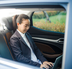 Close up portrait of a young business woman using Laptop in the back seat of the car.