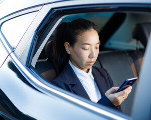 Close up portrait of a young business woman using mobile phone in the back seat of the car.