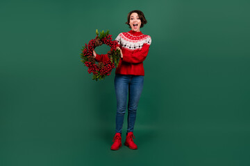 Full length body size view of attractive cheerful amazed girl holding festal eve wreath isolated over green color background