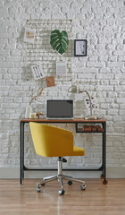 Decorative working room with brick wall, chair, laptop and home office style. Wooden desk with lamp style.