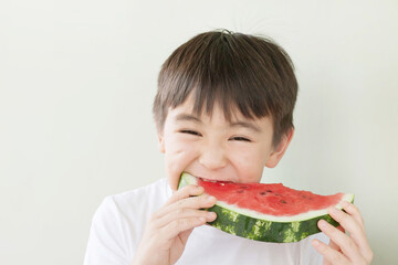 Happy cute asian child boy eating red watermealon indoors
