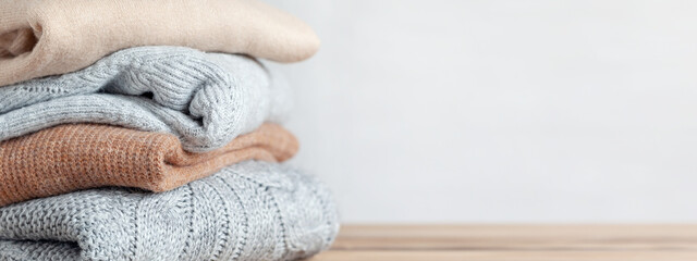 Pile of cozy knitted sweaters on a neutral background. Warm concept