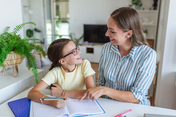 Mother Helping Her Daughter While Studying at home. Pretty smiling woman helping adorable daughter doing schoolwork at home