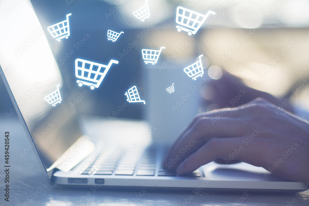 Poster Close up of hands using notebook with abstract glowing cart icons on blurry background. Online shopping, e-commerce and purchase concept.