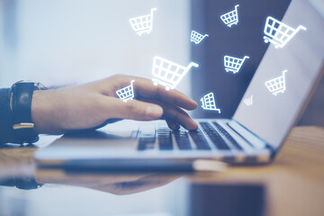 Close up of hands using laptop computer with abstract glowing cart icons on blurry background. Online shopping, e-commerce and purchase concept. © Who is Danny