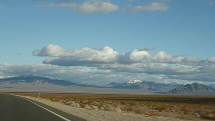 Road trip, driving auto from Death Valley to Las Vegas, Nevada USA. Hitchhiking traveling in America. Highway journey, dramatic atmosphere, clouds, mountain and Mojave desert wilderness. View from car