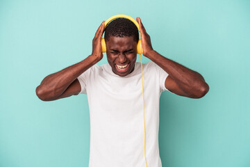 Young African American man listening to music isolated on blue background covering ears with hands.