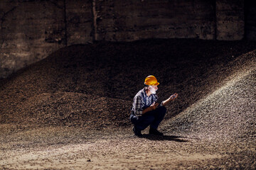 An old bearded worker is crouching in a dark room full of sugar beet products and checking on...