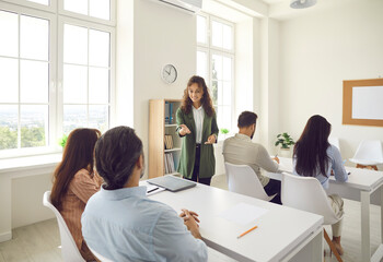 Friendly female teacher communicates with a group of adult students at a seminar in advanced training.Women and men in the classroom.Concept of corporate course marketing strategy and adult education