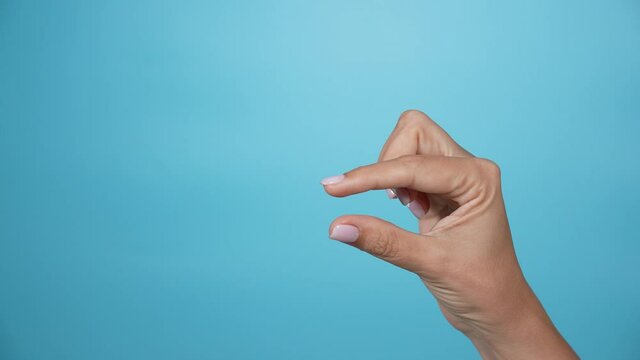Close-up view 4k stock video footage of 1 female hand forming gesture as if showing big and small sizes of virtual invisible object with help of two fingers isolated on bright blue color background
